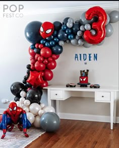 a room with balloons and spiderman decorations on the wall, along with a desk