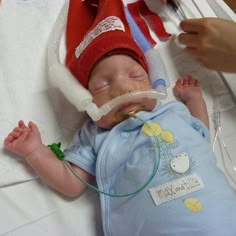 a baby wearing a red hat laying on top of a hospital bed with an oxygen tube in it's mouth