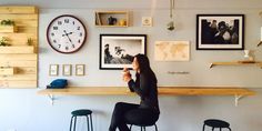 a woman sitting at a bar in front of a wall with pictures and clocks on it