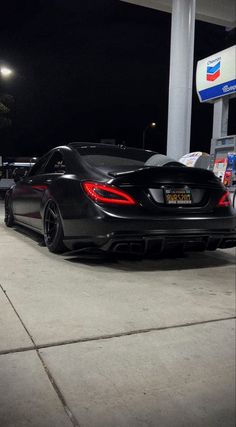 a black sports car parked in front of a gas station at night with its lights on