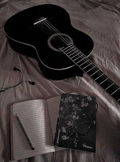 an acoustic guitar, notebook and pen on a bed