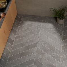 a kitchen with grey herringbone tile flooring and wooden cabinetry next to a potted plant