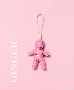 a pink teddy bear ornament hanging from a string on a pink background with the words ginger up