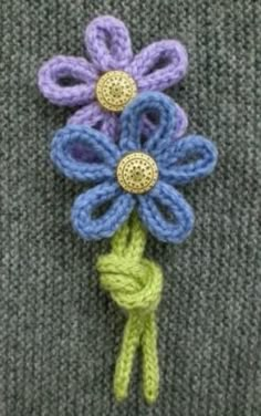 a crocheted flower on top of a gray sweater with green and blue yarn