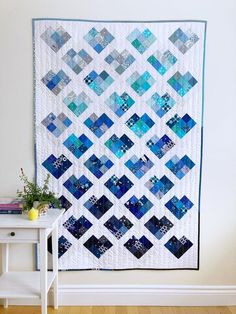 a blue and white quilt hanging on the wall next to a small table with a potted plant