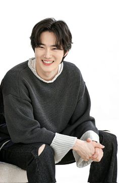 a young man sitting on top of a white chair wearing a sweater and black pants