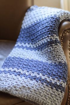 a blue and white crocheted blanket sitting on top of a brown leather chair