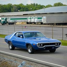 a blue muscle car driving down the road