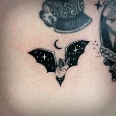 a bat tattoo on the back of a woman's shoulder, with stars and a clock in the background