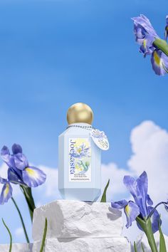 a bottle of perfume sitting on top of a white block with purple flowers in the background