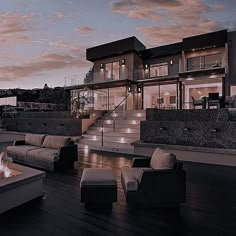 a fire pit sitting on top of a wooden deck next to a large house at dusk