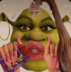 a woman with green makeup and pink nails holding a candy bar in front of her face