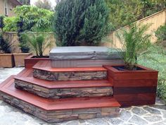 a hot tub sitting on top of a wooden deck next to plants and trees in a backyard