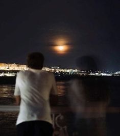 two people looking out over the water at night, with a full moon in the background