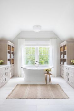 a white bathroom with a large tub in the center and lots of cabinets on either side