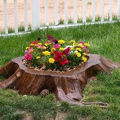 a flower pot sitting on top of a tree stump in the grass next to a fence