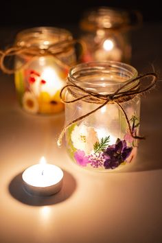 three glass jars with flowers on them and a lit candle