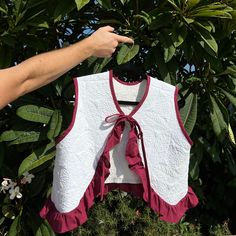 a woman's hand pointing at a white and red top hanging from a tree