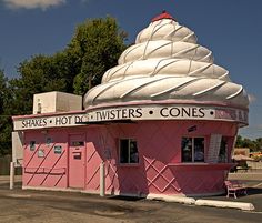 a pink and white building sitting in the middle of a parking lot next to trees