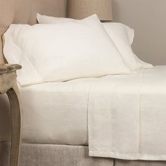 the bed is made with white linens and pillows on top of it, along with a side table