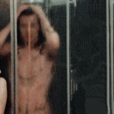 a blurry image of a naked woman looking through a glass door with her hands behind her head