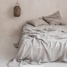 an unmade bed with grey linens and a basket hanging on the wall above it