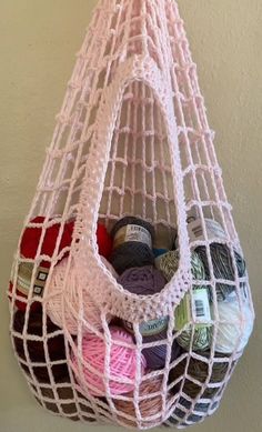 a white net bag filled with yarn and balls of thread hanging from a hook on the wall