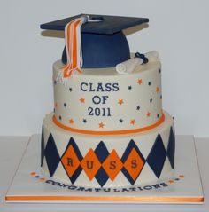 a graduation cake is decorated with an orange, blue and white ribbon on top of it