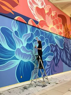 a woman painting a mural on the side of a building with flowers painted on it