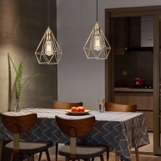 a dining room table with four chairs and two pendant lights hanging from the ceiling above it