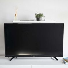 a flat screen tv sitting on top of a white dresser next to a plant and books