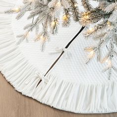 a white christmas tree skirt on top of a wooden table with pine branches and lights