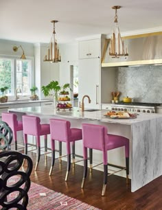 a kitchen with marble counter tops and pink chairs in front of an island that has gold accents