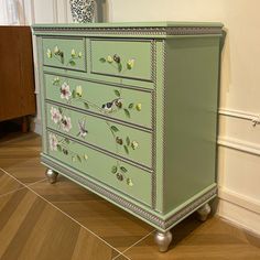 a green dresser with flowers painted on the front and sides, sitting in a room