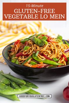 a black bowl filled with noodles and vegetables on top of a white table next to green beans