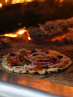 a pizza sitting on top of a wooden table next to an open fire oven door