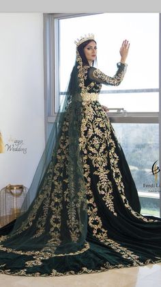 a woman in a black and gold wedding dress standing next to a window with her hands up