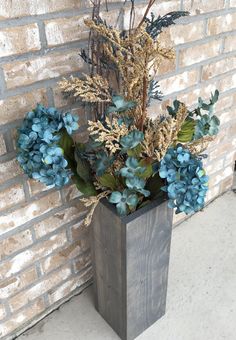 a wooden vase filled with blue flowers next to a brick wall