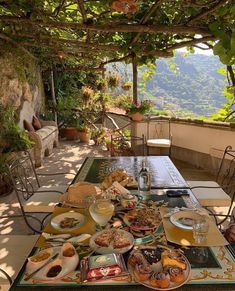 an outdoor table with food and drinks on it in front of a stone wall covered patio