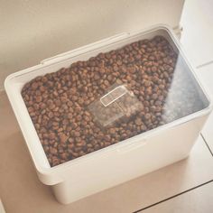 a plastic container filled with dog food on top of a white tiled floor next to a wall