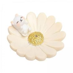 a small white cat sitting on top of a flower with a gold ball in it's mouth