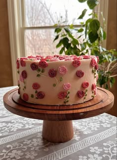 a cake with pink frosting and roses on it sitting on a wooden platter