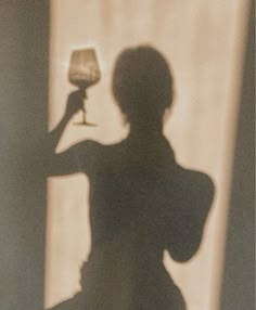 the shadow of a woman holding a wine glass in front of her face and arm