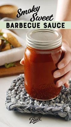 a person holding a jar of barbecue sauce on top of a cloth with the words smoky sweet barbecue sauce above it