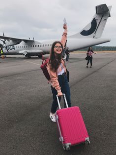 a woman is standing with her luggage in front of an airplane on the tarmac