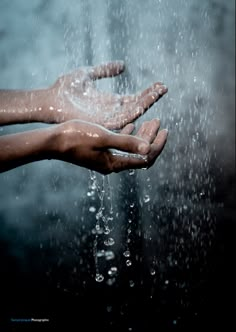 two hands reaching out to the water coming from under their arms, with rain falling down on them