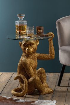 a monkey sitting on its hind legs with a glass table top that has whiskey glasses on it