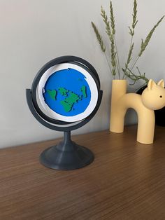 a small blue and green globe sitting on top of a wooden table next to a plant