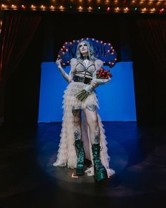 a woman dressed in costume standing on stage with lights behind her and holding flowers up to the side