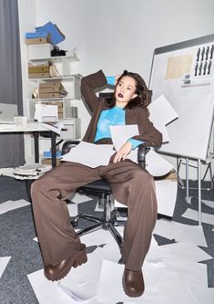 a woman is sitting in an office chair with papers on the floor and holding her head